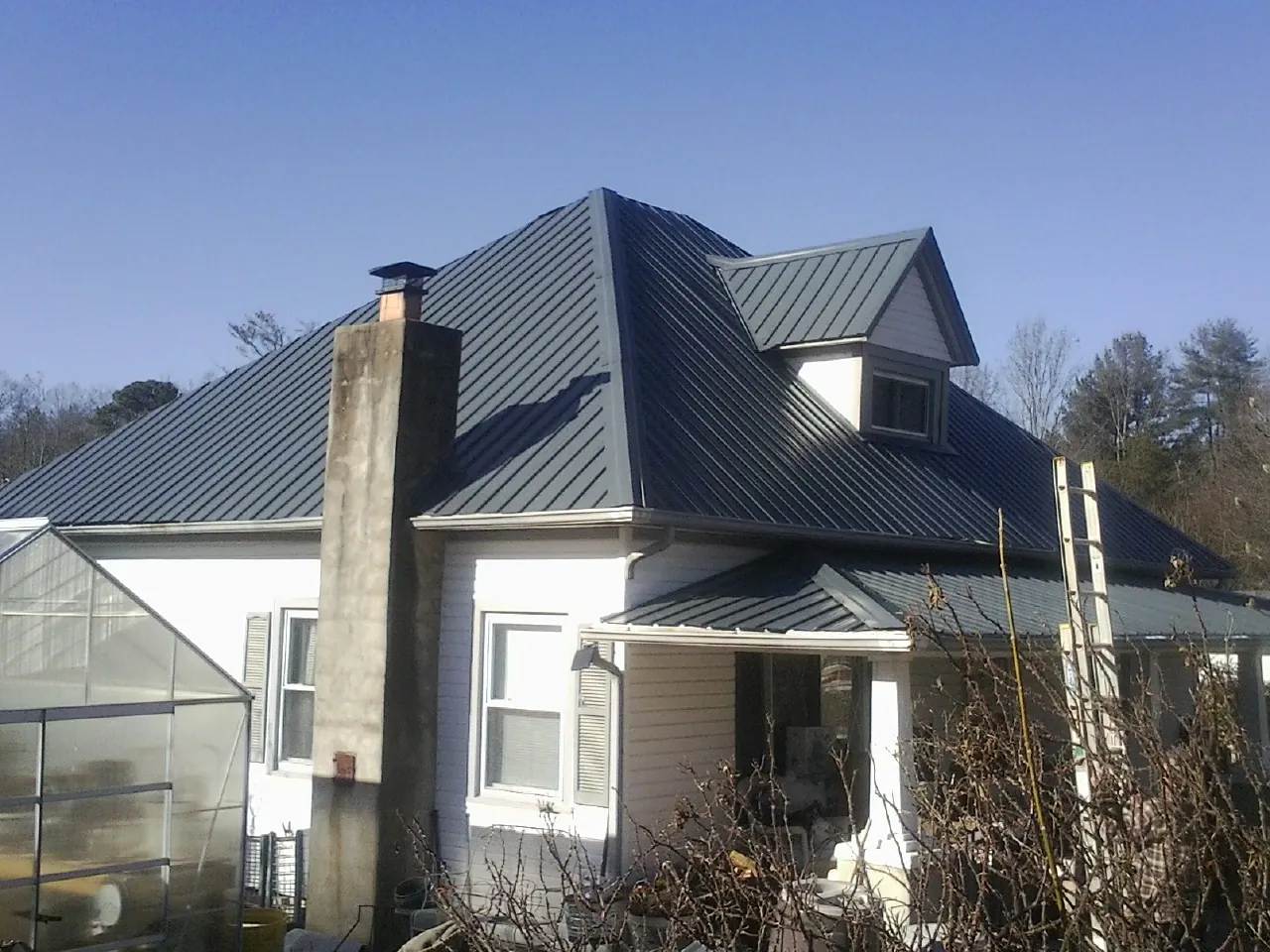 Dark blue standing seam metal roof on a white farmhouse with dormer — Slate & Tile Roof Repair by Roofing Brothers in South Byron