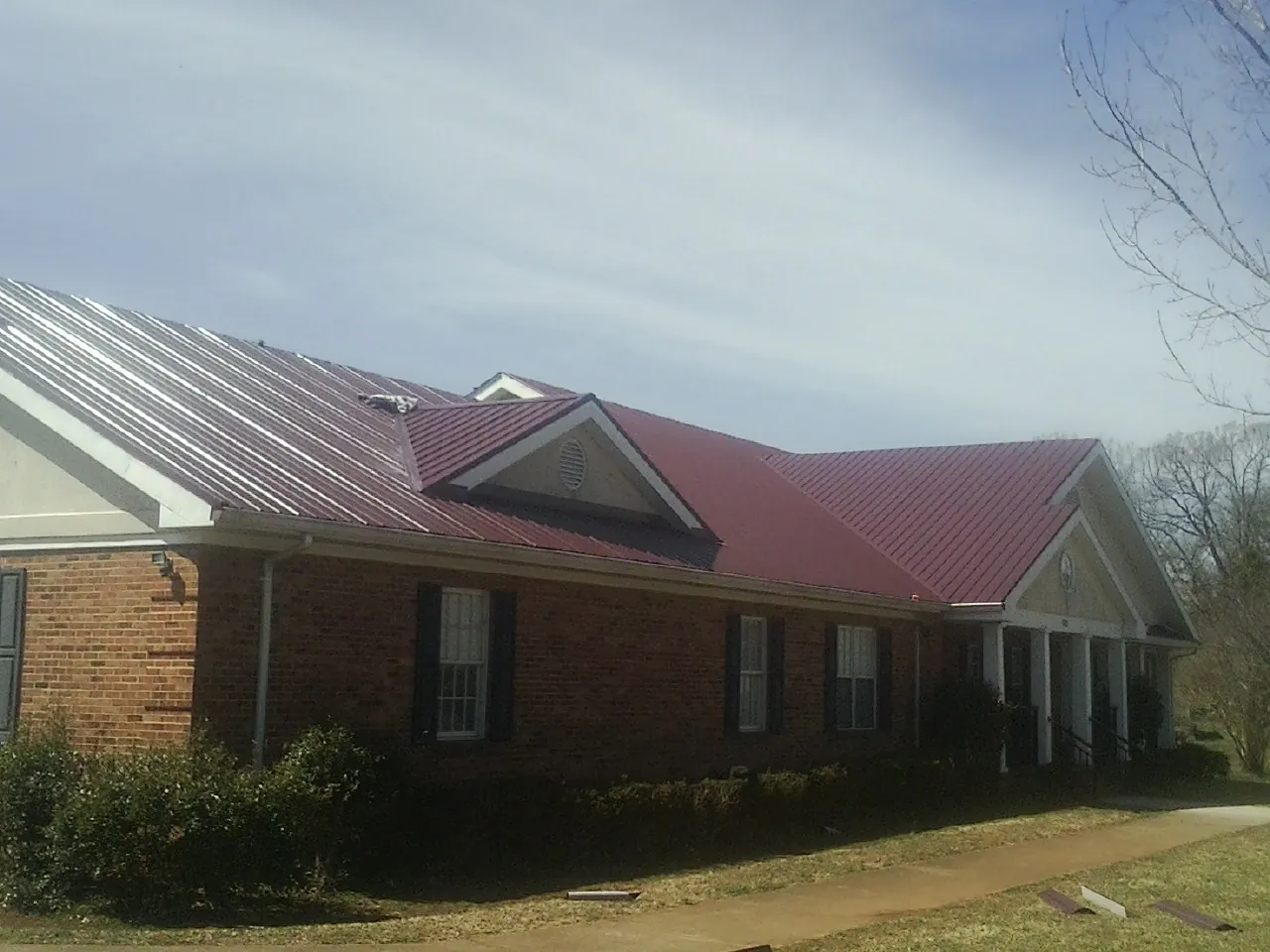 Red metal roof with gabled entries on a long brick building, from a Hail Damage Roof Repair job in South Byron