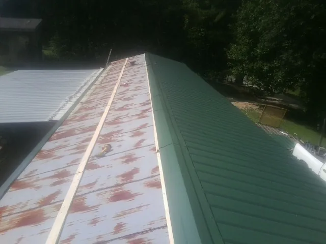 Old rusted panels beside newly installed green metal roofing — Wind Damage Roof Repair by Roofing Brothers in South Byron