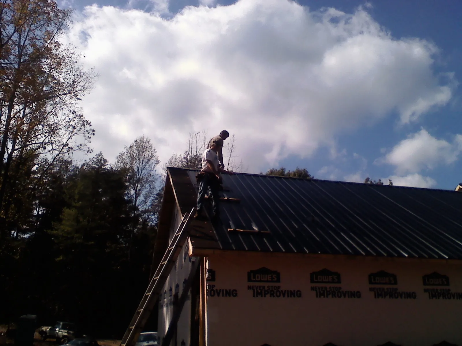 Roofer fastening dark metal panels high against a cloudy sky, from a Roof Inspection job in South Byron
