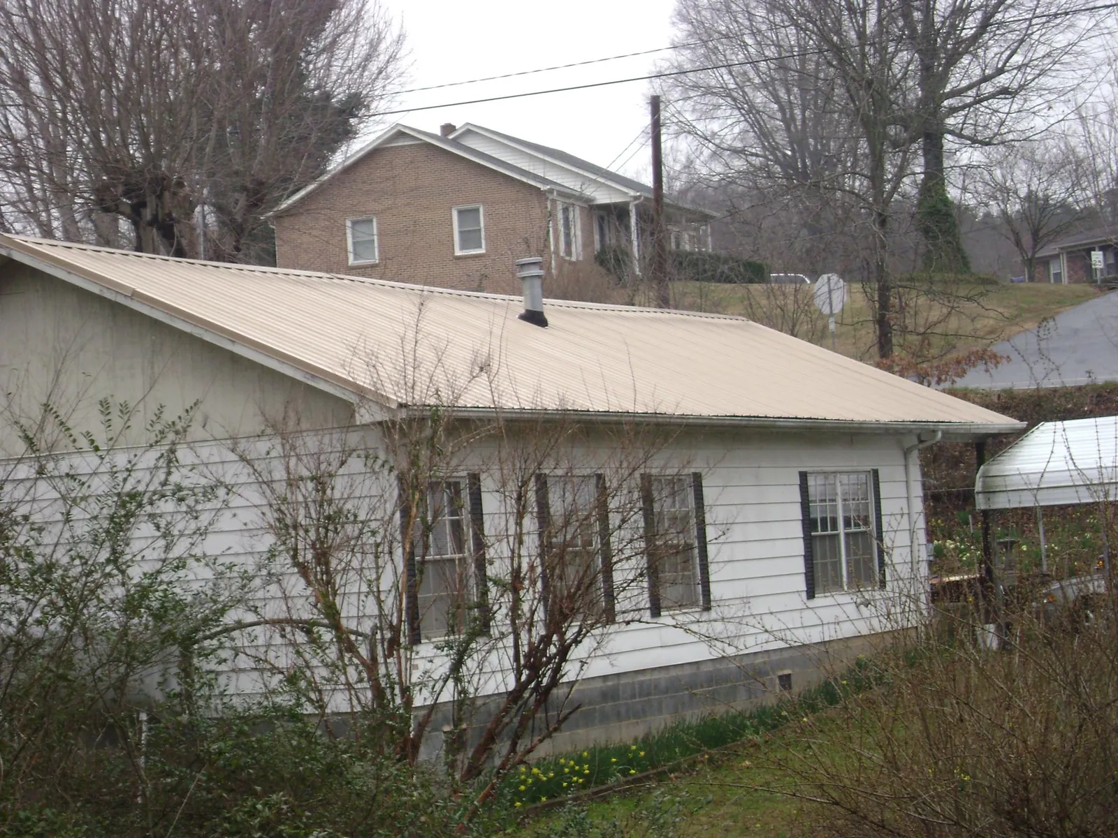 Tan metal roof on a white sided house set into a hillside — Commercial Roofing by Roofing Brothers in South Byron
