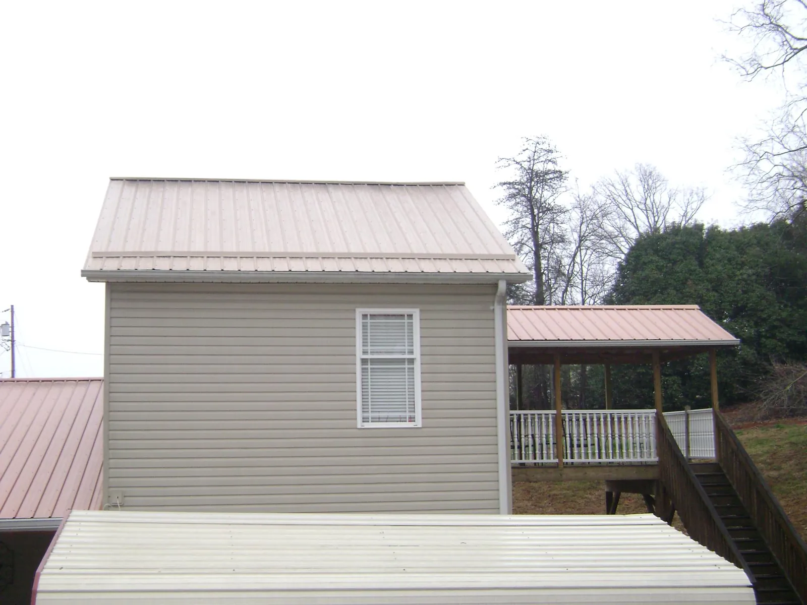 Tan metal roofs on a two story addition and attached porch, from a Roof Replacement job in South Byron